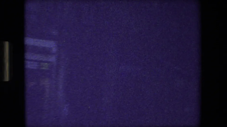 Low-exposure 8mm frame from the Paris vehicle sequence, showing mostly dark purple window view with faint structural or reflected detail.