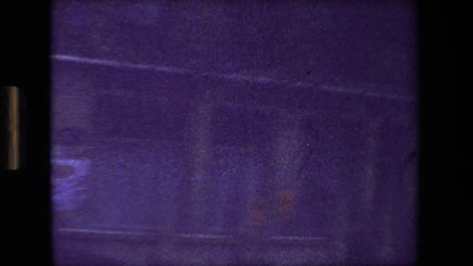 Purple-tinted 8mm frame from the Paris 1981 clip showing a blurred moving-vehicle view with dark borders, faint street reflections, and indistinct building surfaces.