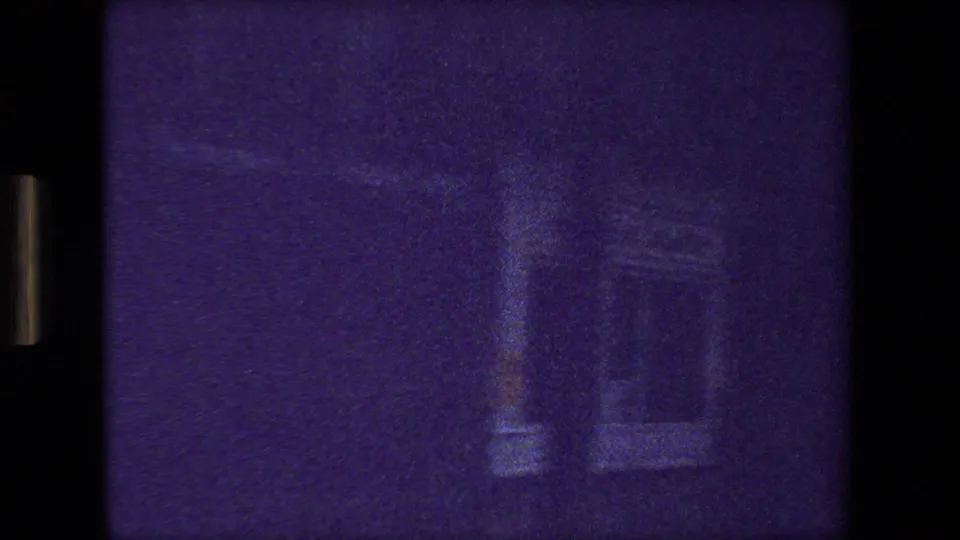 Grainy 8mm frame from the Paris 1981 moving-vehicle clip showing faint vertical building or street-side shapes under a strong purple color shift.