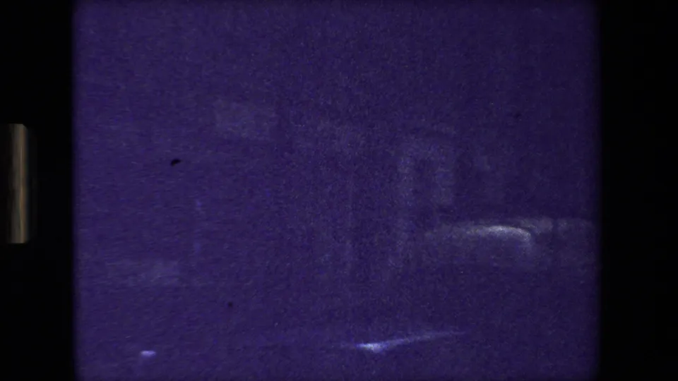 Purple-tinted Paris 1981 8mm frame with indistinct street or building forms, bright lower-edge light streaks, and visible analog grain.