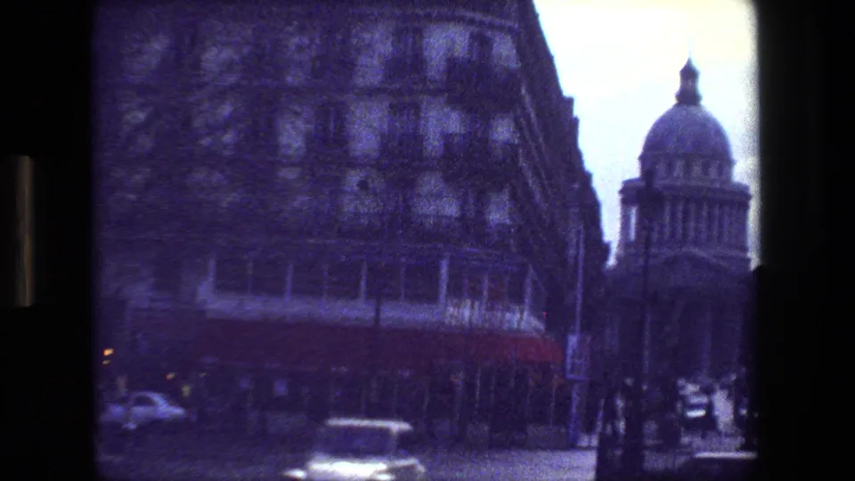 1981 Paris home-movie frame looking along a city street toward a domed classical building, with surrounding urban facades and cars in the foreground.