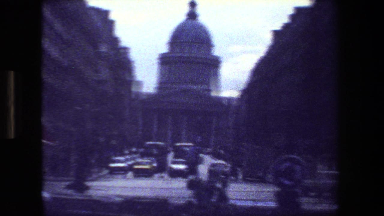 Domed building beyond a street with cars, trees, and deep shadows.