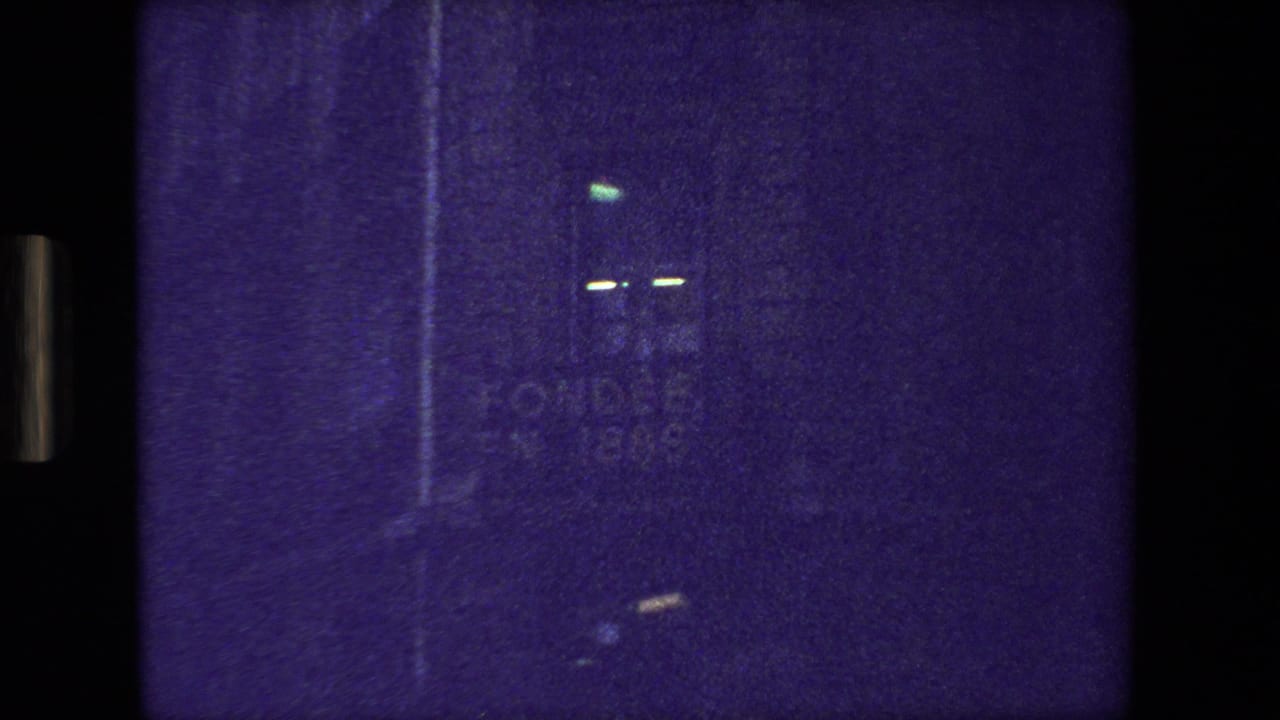 Dark purple-tinted 8mm frame from the supplied 1981 Paris clip, showing indistinct light marks, film grain, and black projection borders.