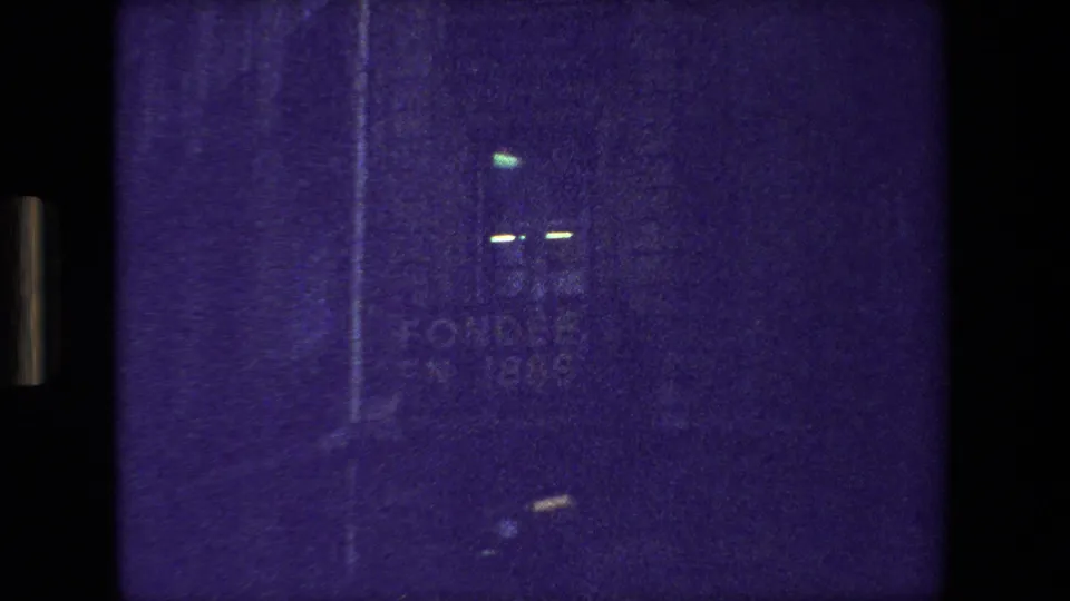 Dark purple-tinted 8mm frame from the supplied 1981 Paris clip, showing indistinct light marks, film grain, and black projection borders.