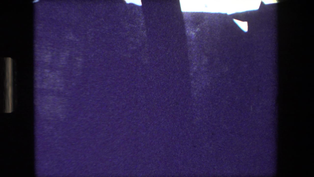 Mostly dark purple film frame with black vertical borders and a bright area at the top edge.