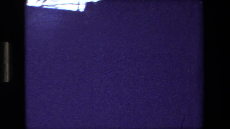 Purple-tinted 8mm frame from the moving sequence, with an overexposed upper strip, dense grain, and minimal readable exterior detail.