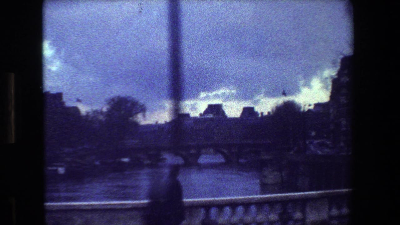 River view with arched bridge, distant buildings, cloudy sky, and stone railing.