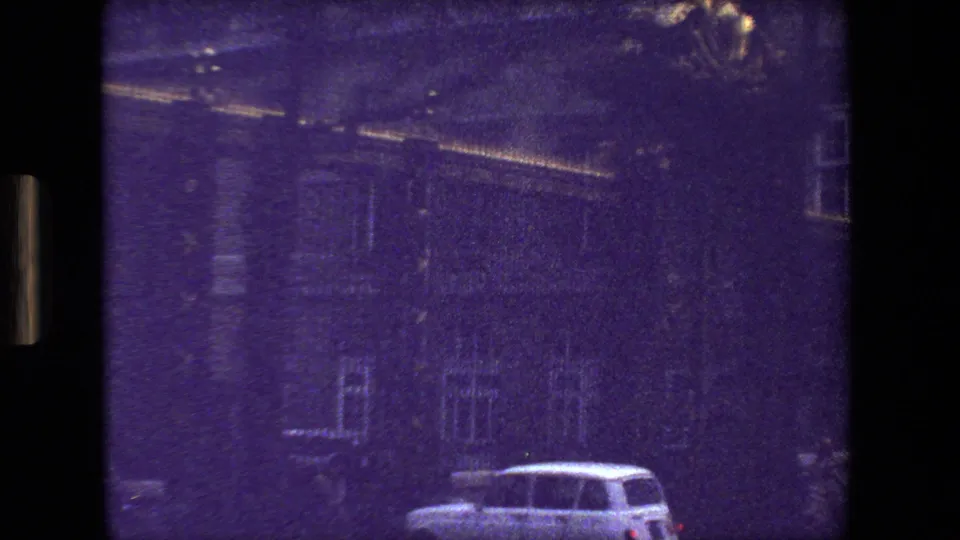 1981 Paris 8mm frame showing a soft, purple-shifted view of a grand stone facade behind fencing, with a light-colored car partially visible near the lower edge.