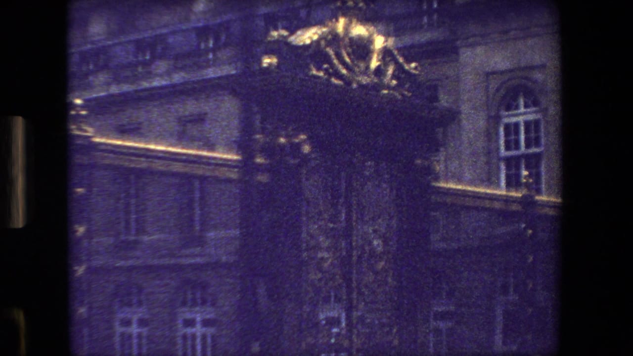 Gilded ornamental crest above dark iron gates in front of a large stone building.