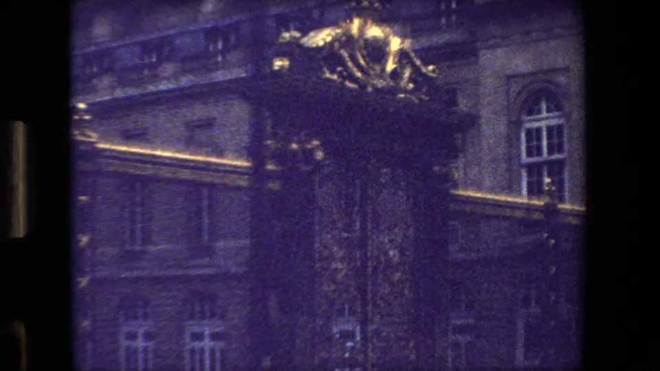 1981 Paris 8mm frame with gilded ornament and dark iron gates in front of a large stone building with arched windows, seen from a moving viewpoint.