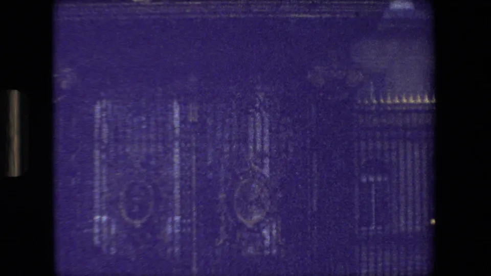 1981 Paris 8mm frame showing wrought-iron gates, a large stone facade, and gilded ornament near the upper edge, with strong purple cast and low contrast.