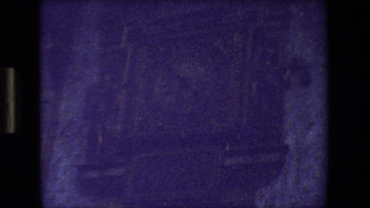 Dark, blue-tinted 8mm frame with indistinct vertical forms and film gate edges.