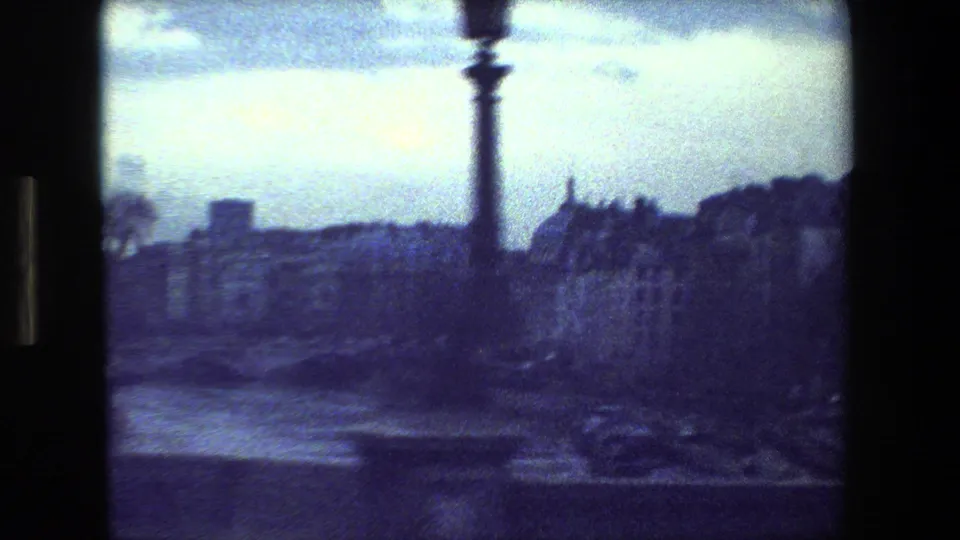 1981 Paris 8mm frame showing a hazy riverside city view with buildings, a broad river, cloudy sky, and a dark vertical street fixture near the center.