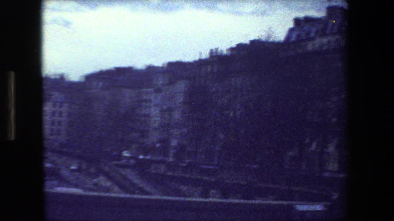 1981 Paris home-movie frame with a wide river in the foreground, dense riverside buildings, leafless trees, and a pale overcast sky.