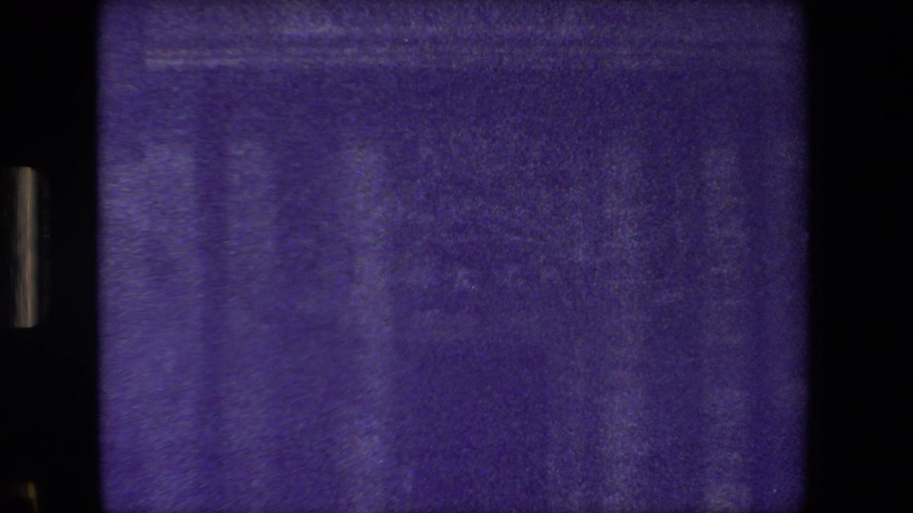 Purple-shifted 8mm frame from the Paris home-movie clip showing a dark masonry facade with faint windows and visible film border artifacts.