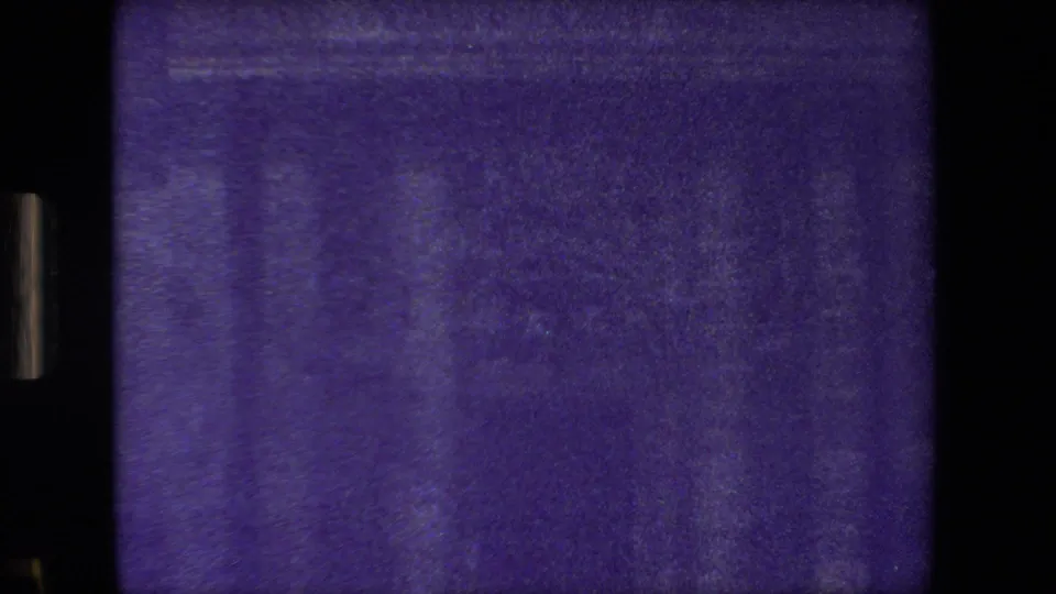 Purple-shifted 8mm frame from the Paris home-movie clip showing a dark masonry facade with faint windows and visible film border artifacts.