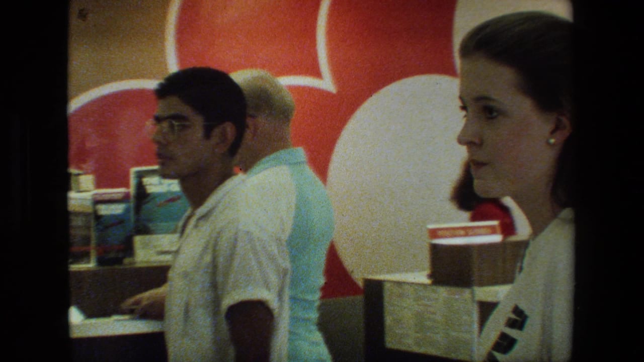 A woman stands near the airport counter while passengers wait beside a red-and-white wall graphic.