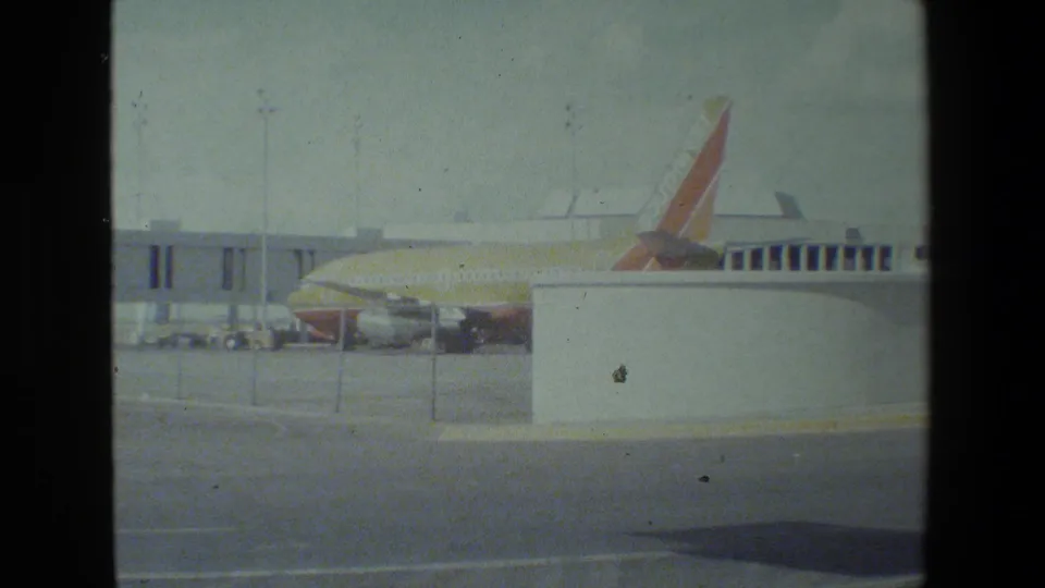 A Southwest-liveried jet is partly hidden by a white foreground structure, with the terminal jet bridge, service area, and apron pavement visible around it.