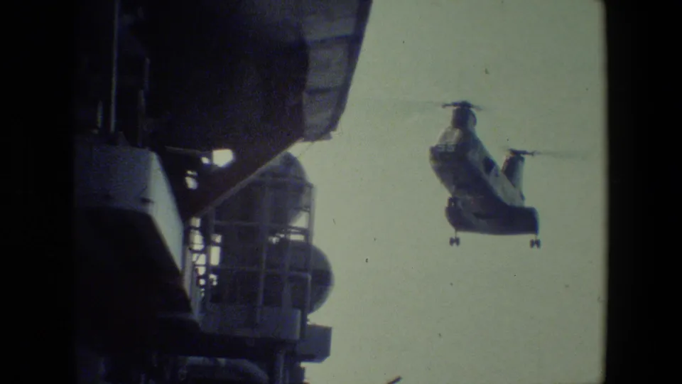 The helicopter appears closer and lower beside the ship superstructure, with both rotors visible against the pale sky in the final frame.