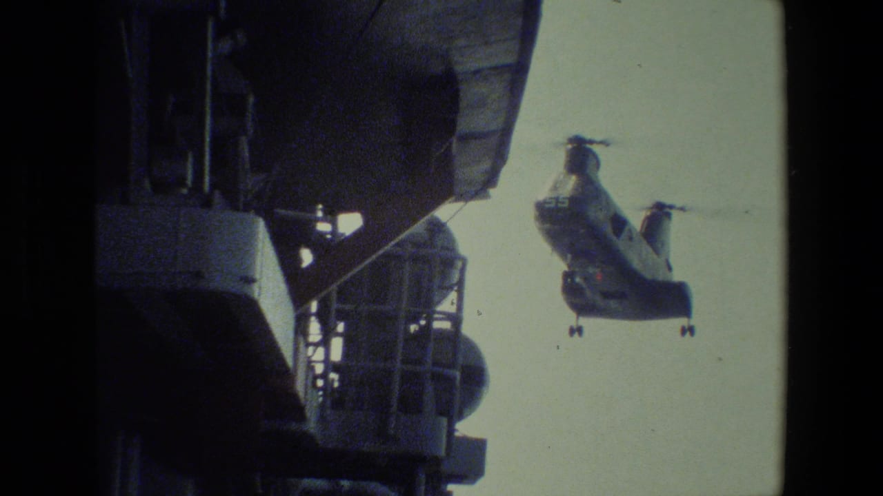 A large military-style twin-rotor helicopter approaches beside visible ship superstructure in grainy 8mm home-movie footage from the supplied 1981 clip.