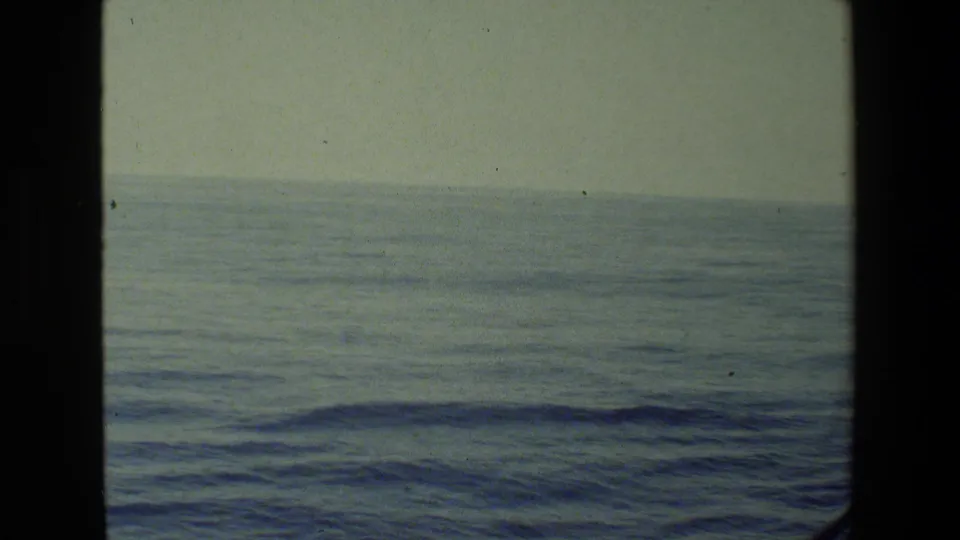 The camera frames the open sea and low horizon in soft, color-faded 8mm footage, with no person visible in this extracted still.