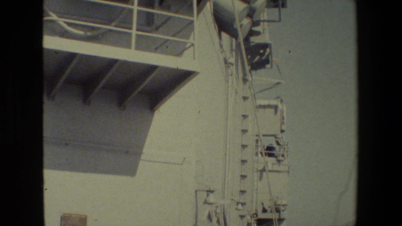 1981 8mm frame showing a close, upward view of a white naval vessel superstructure with railings, platforms, and mounted equipment.