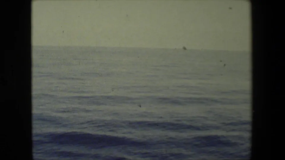 Shipboard 8mm view across open ocean, showing low rolling waves, a flat horizon, pale sky, and the dark divider of the contact-sheet scan.