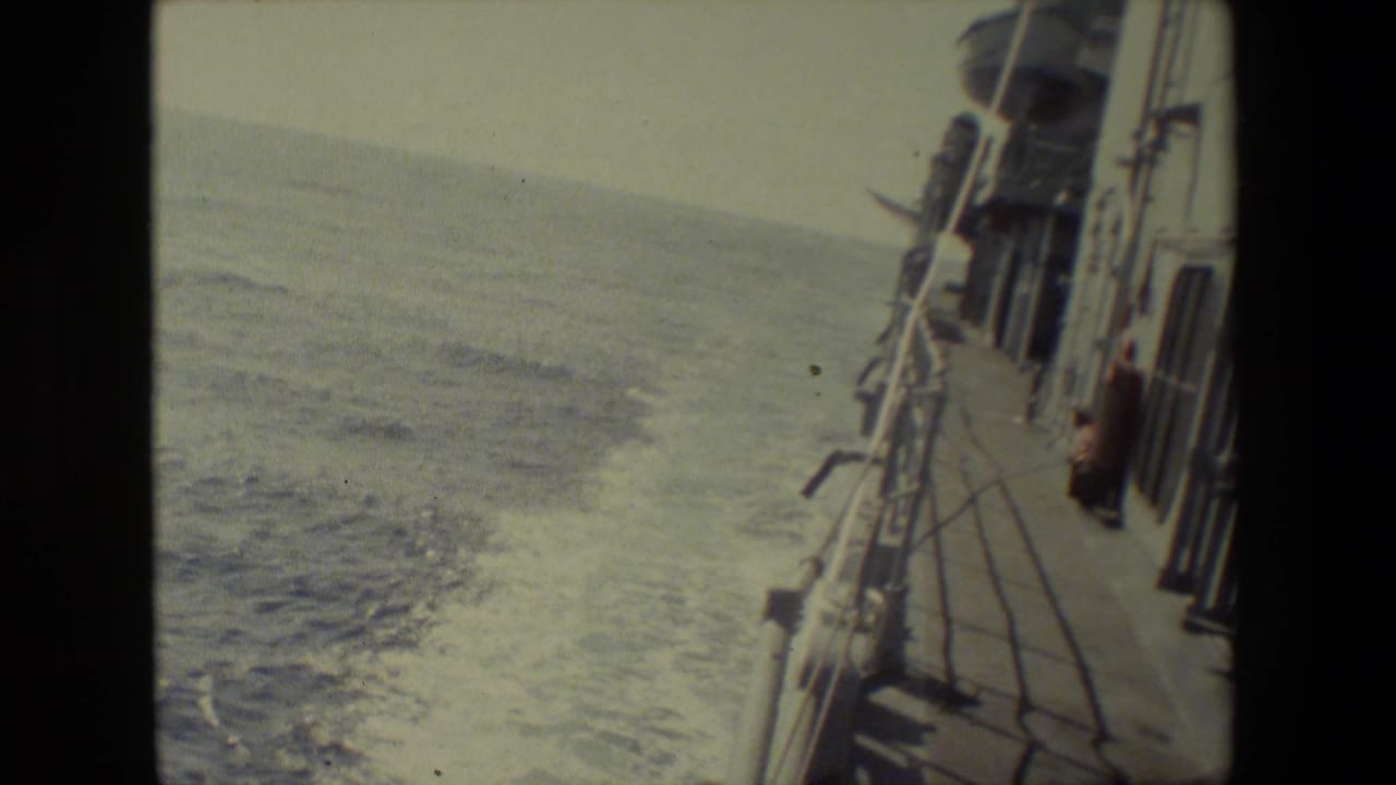 The vessel's side deck and railings run along the right side of the frame while foamy wake spreads across the open water.