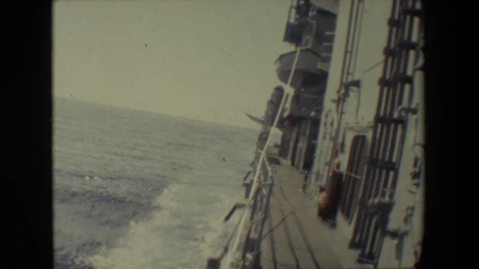 A tilted 8mm frame shows the ship's side deck, railings, vertical fittings, and white wake running along the vessel in open water.