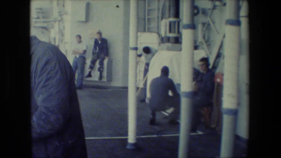 Ship deck scene with several men in work clothes or uniforms near vertical pipes, posts, ladders, and deck equipment, consistent with the supplied San Diego Naval Base metadata.