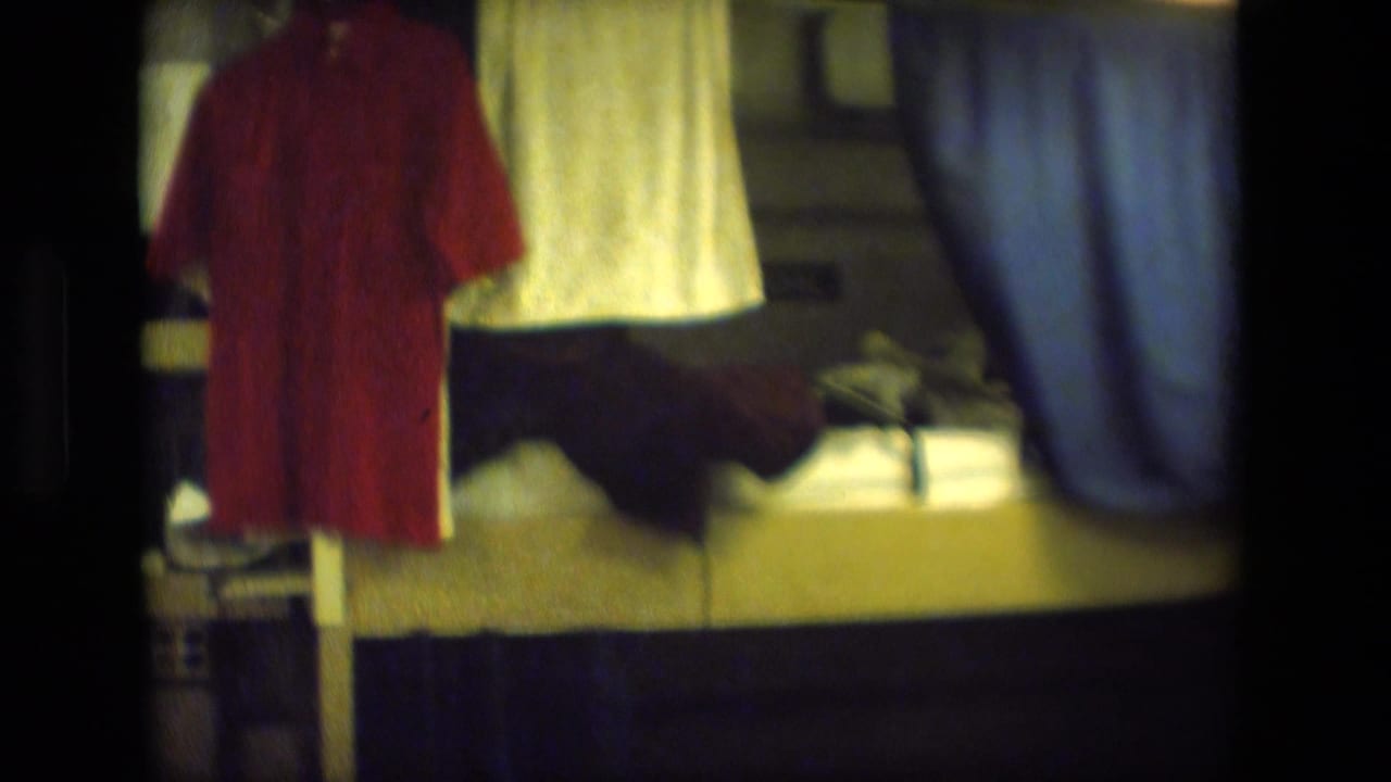Hanging red shirt, white towel, bedding, and blue curtain inside a small room.