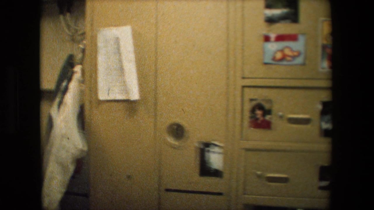 Close view of tan lockers inside a Navy ship space, with taped papers, small personal photos, and a light garment hanging at the side.