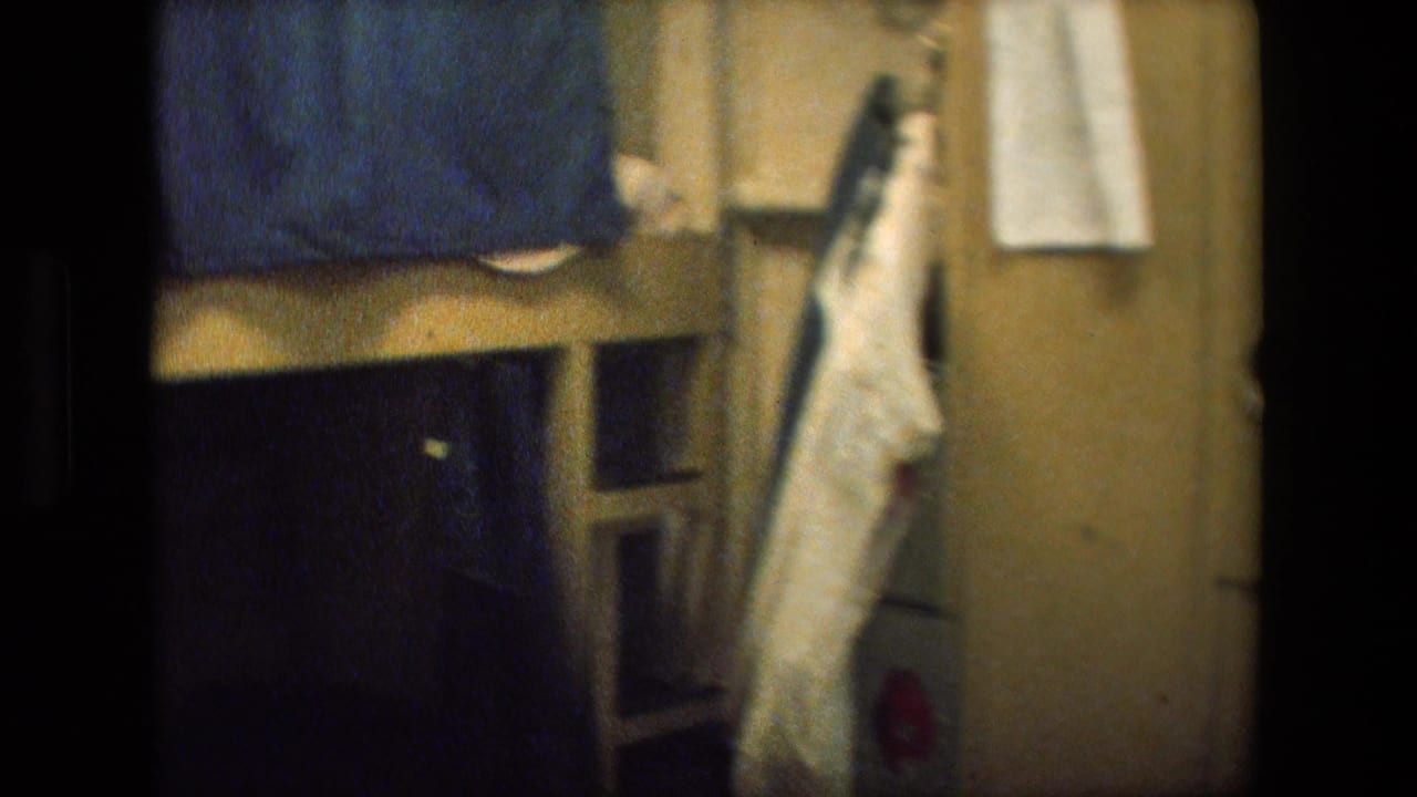 Bunk area with blue fabric, hanging clothing, and built-in storage inside a ship compartment.