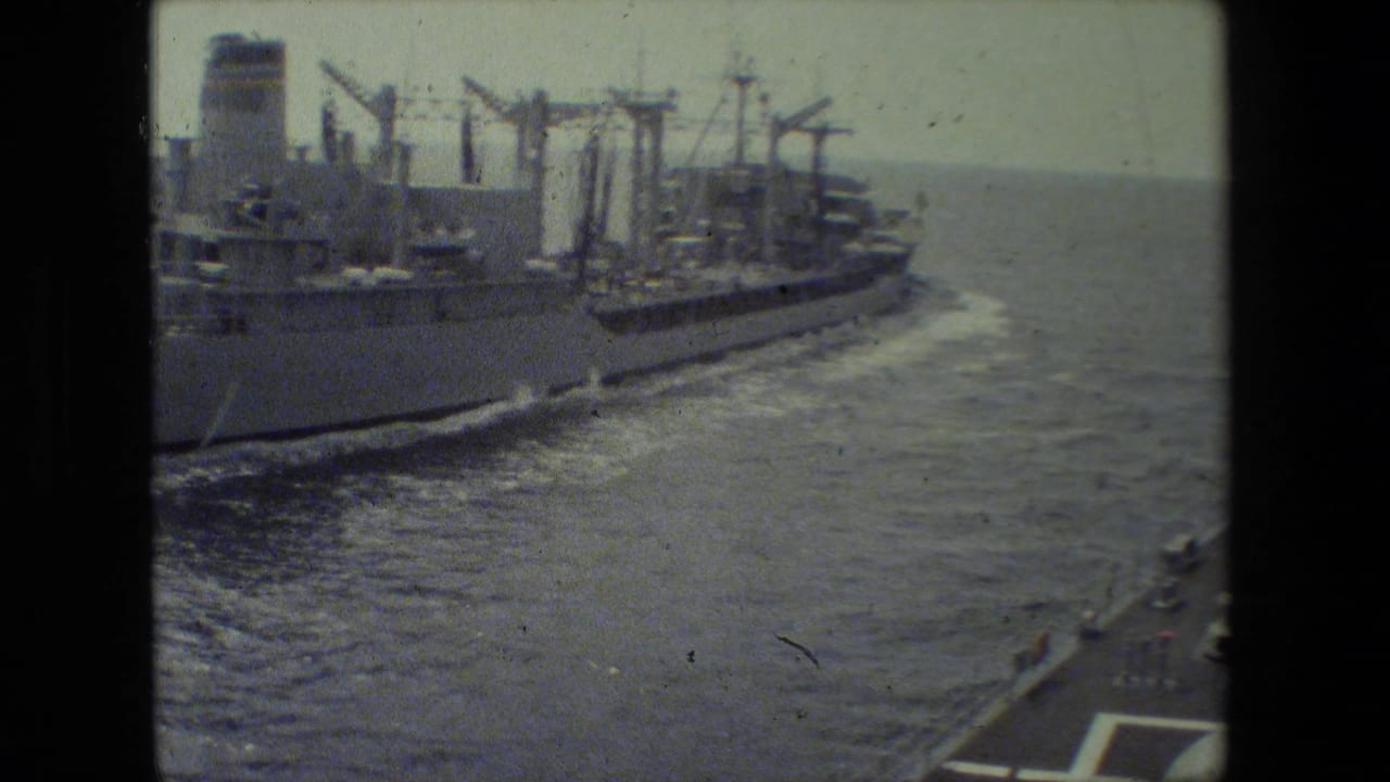 A large naval cargo or support ship appears alongside open ocean, filmed from a moving vessel in supplied 1981 8mm home-movie footage.