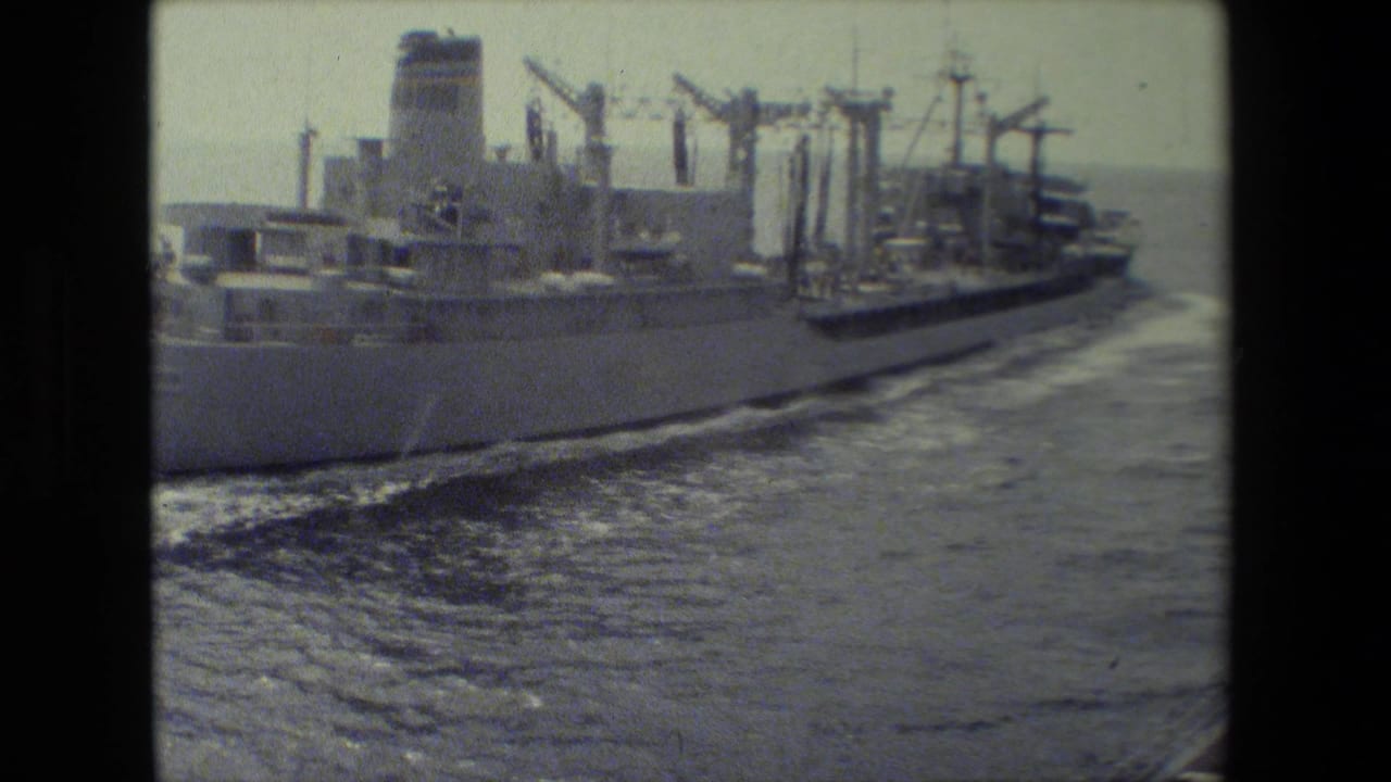 Side view of a large ship moving through open water with wake behind it.