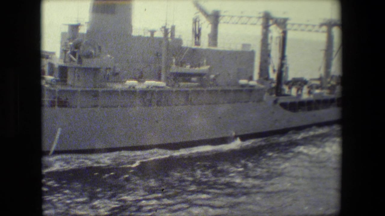 Military ship midsection with cranes and wake visible.