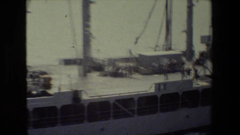 A closer view of the vessel deck shows railings, masts, clustered equipment, and a few small figures near the ship's side.