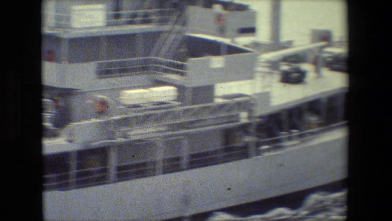Soft 8mm frame showing the side of a white ferry or transport vessel with deck railings, equipment, and foamy water washing along the hull.