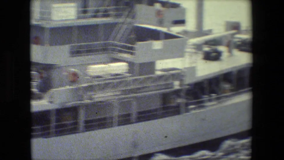 Soft 8mm frame showing the side of a white ferry or transport vessel with deck railings, equipment, and foamy water washing along the hull.