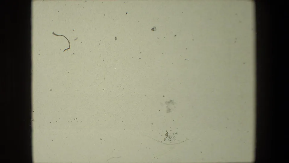 Mostly overexposed or blank 8mm frame with pale color, dust specks, scratches, and the contact-sheet border visible.