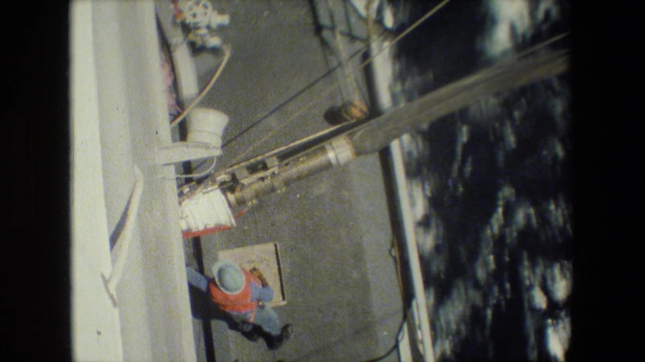 Worker in an orange vest on a ship deck near rigging and rough water.