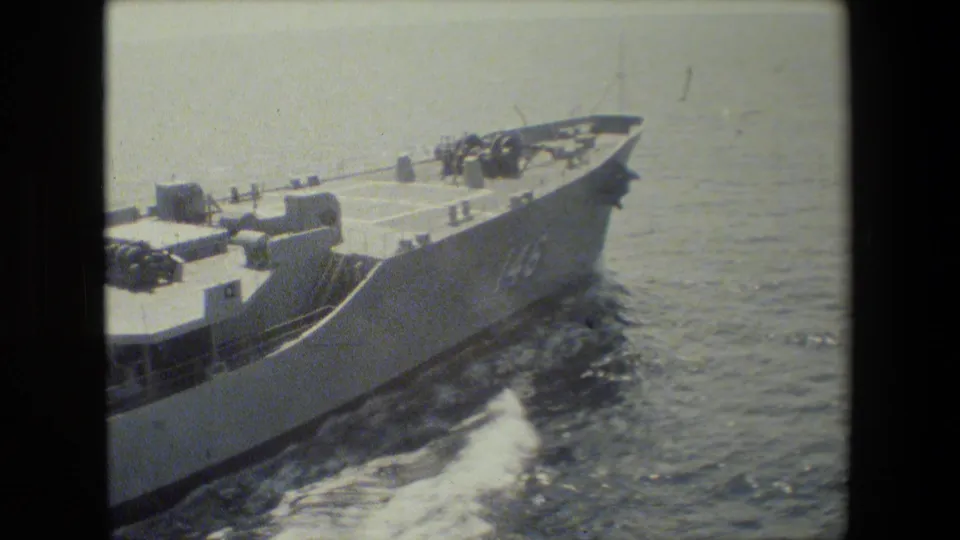The bow and forward deck of a gray naval-looking vessel pass close to the camera ship, with water spray and soft color-faded 8mm texture visible.