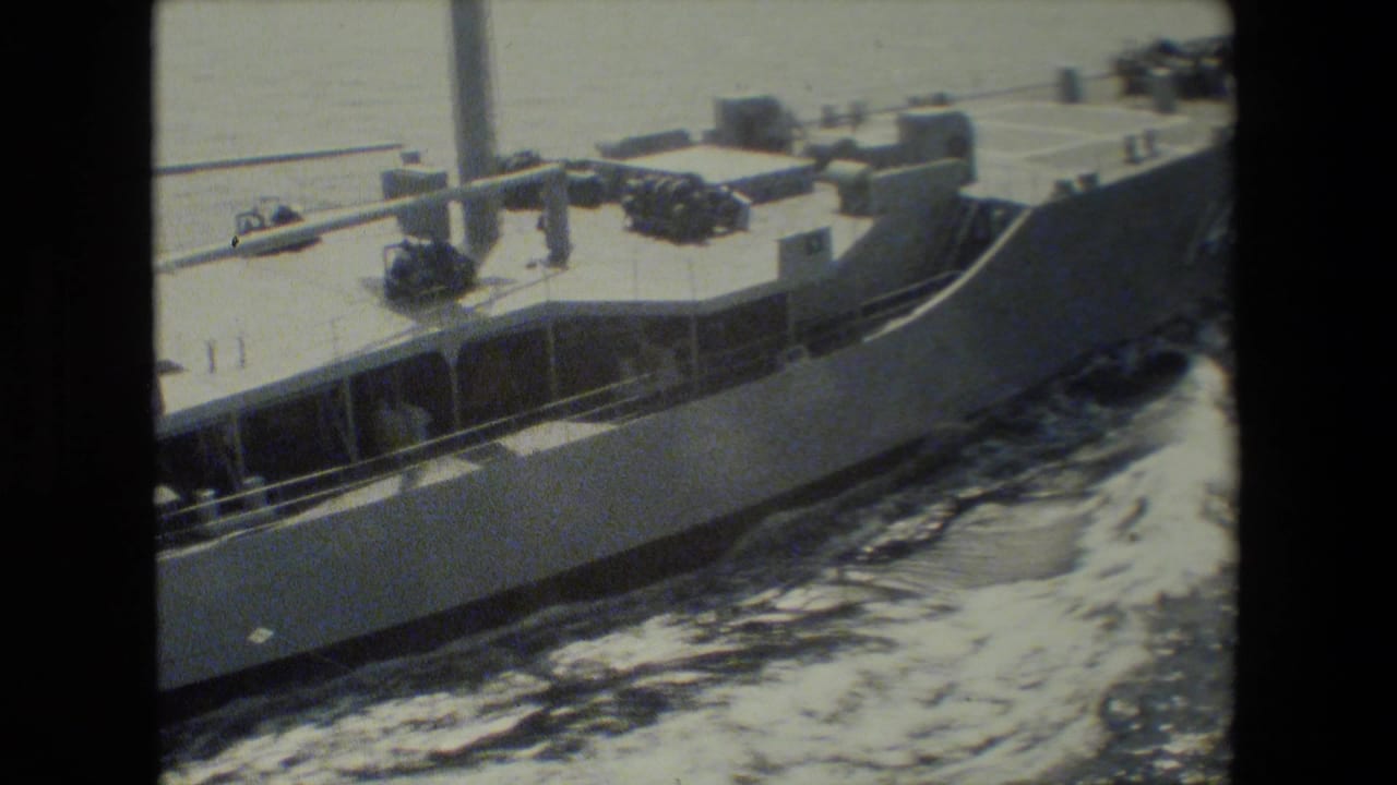 1981 San Diego Naval Base home-movie frame showing a U.S. Navy ship’s hull, deck railings, and water wake from a close, elevated viewpoint.