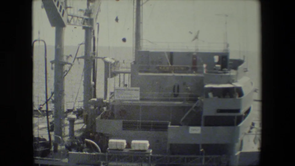 Close 1981 home-movie view of a U.S. Navy ship superstructure with mast hardware, railings, bridge windows, and deck equipment visible.