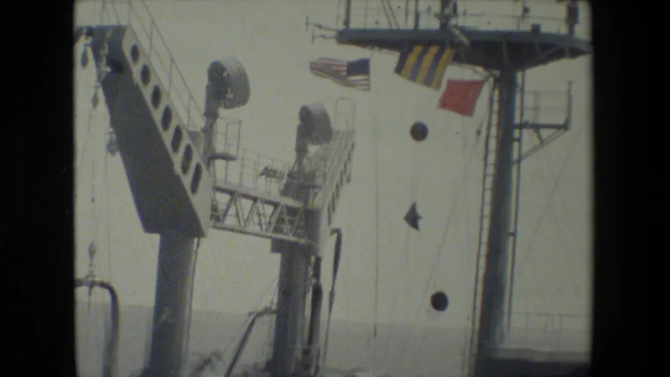 Home-movie frame from the 1981 San Diego Naval Base clip showing signal flags, rigging, mast structures, and shipboard equipment.