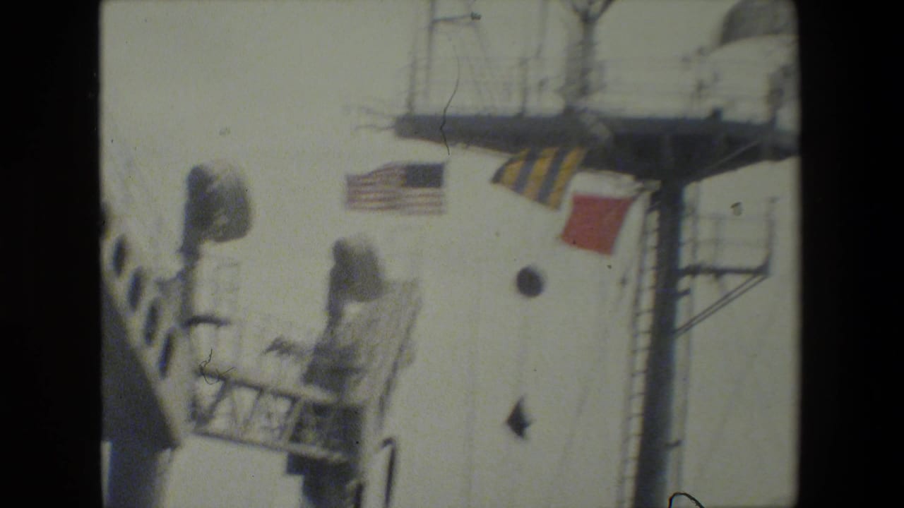 Close view of a ship superstructure with a U.S. flag and signal flags near a mast platform.