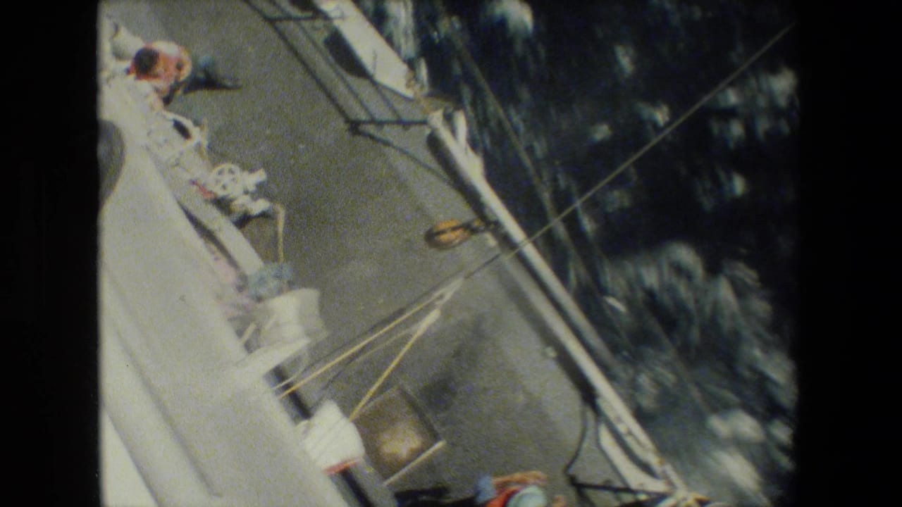 High-angle view along the ship side with rigging lines, deck fittings, and dark water below.
