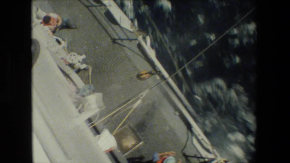 High-angle 8mm view looking down along the side of the vessel, showing rigging lines, deck hardware, and moving seawater below.