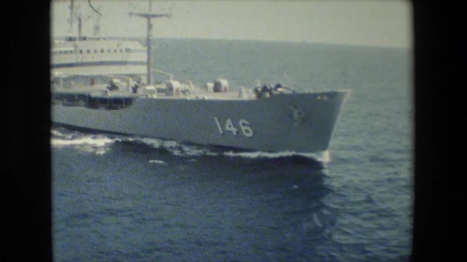 Gray military vessel marked 146 underway on open water, with bow wake, deck structures, and crew or equipment shapes visible along the rail.