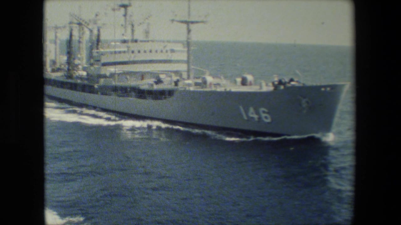 A large white naval vessel with hull number 146 passes across blue open water, with deck equipment, mast structures, and a foaming wake visible in grainy 8mm footage.